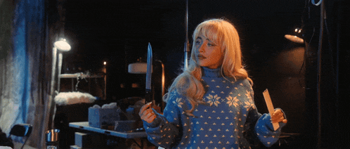 a woman in a blue sweater holds two knives