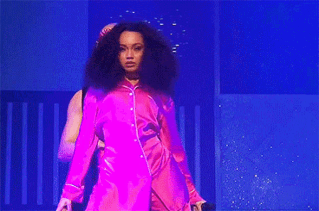 a woman is standing on a stage holding a microphone and wearing a pink pajama suit .