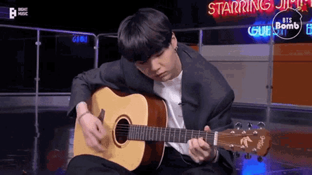 a young man in a suit is playing an acoustic guitar