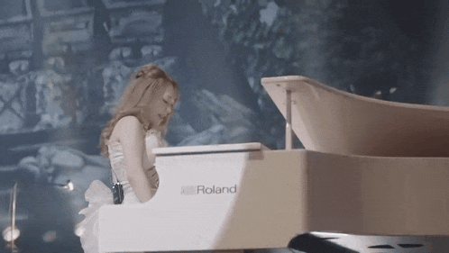 a woman is playing a white roland grand piano