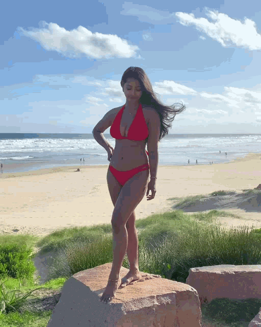 a woman in a red bikini is standing on a rock on the beach