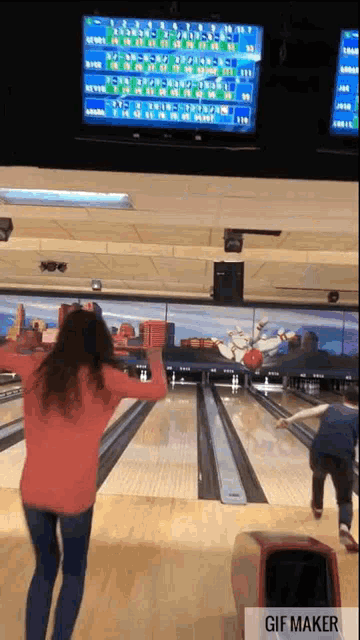 a woman is throwing a bowling ball in a bowling alley while a man watches .