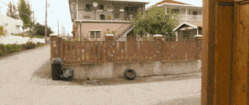 a black garbage bag sits on the sidewalk in front of a wooden fence