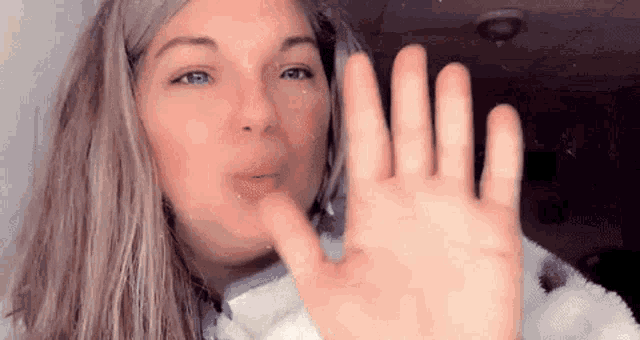 a woman is blowing a kiss while holding her hand up .