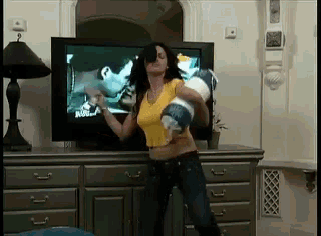 a woman is dancing in front of a television in a living room while holding a pillow .