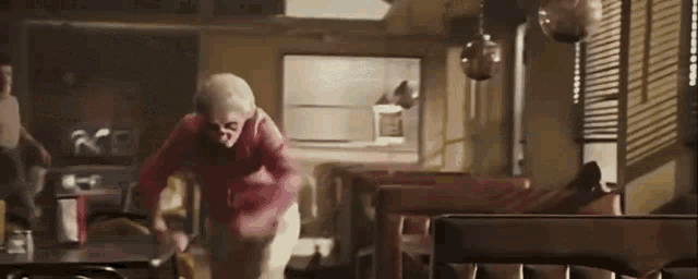 an elderly woman is standing in a diner looking at the camera .