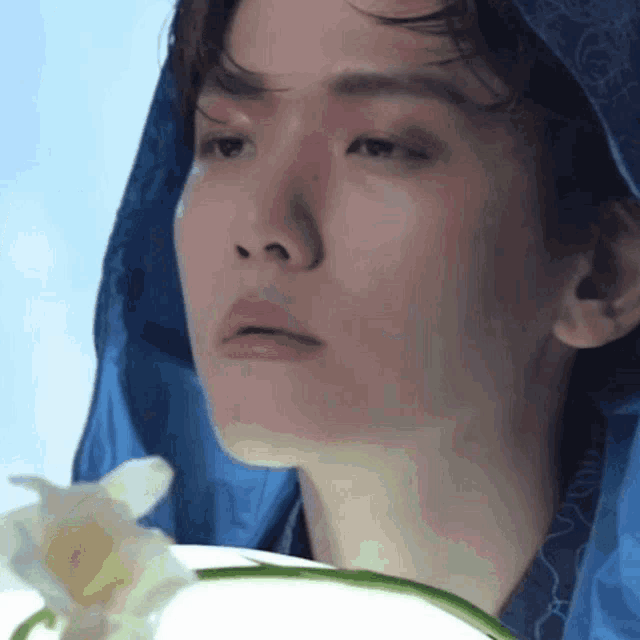 a close up of a person holding a flower and wearing a blue hood .
