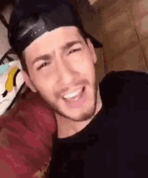 a man wearing a baseball cap and a black shirt is smiling and making a funny face .