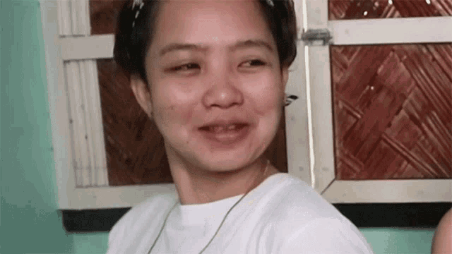 a woman in a white shirt is smiling in front of a wooden door