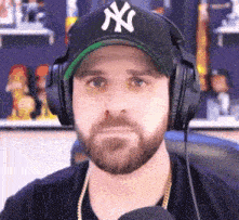 a man wearing headphones and a ny hat looks at the camera