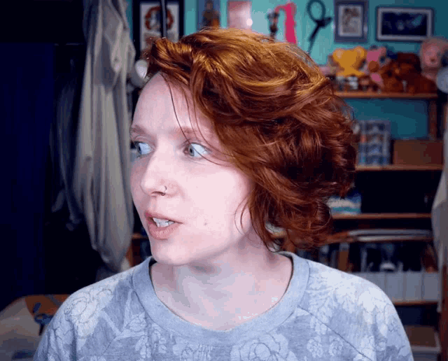 a woman with red hair is wearing a grey floral shirt