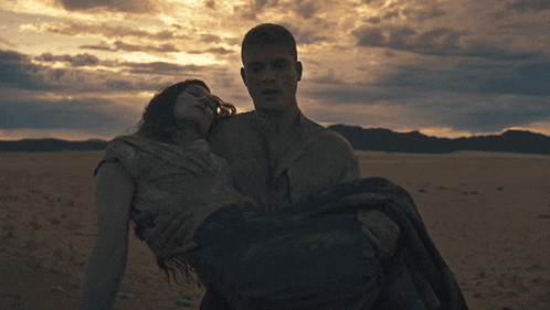 a man carrying a woman in his arms in the desert at sunset
