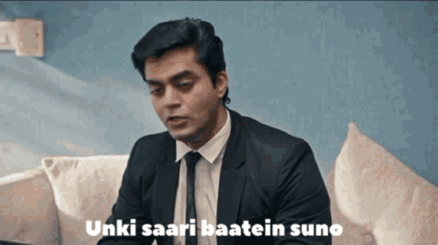 a man in a suit and tie is sitting on a couch with the words " unki saari baatein suno " next to him