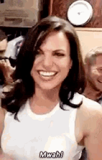 a woman in a white tank top is smiling and says mwah !