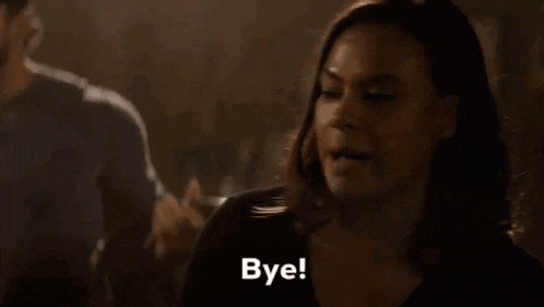 a woman is sitting at a table with a man behind her and says `` bye '' .
