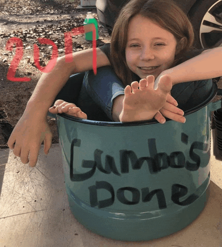 a little girl is sitting in a bucket that says gumbo 's done on it