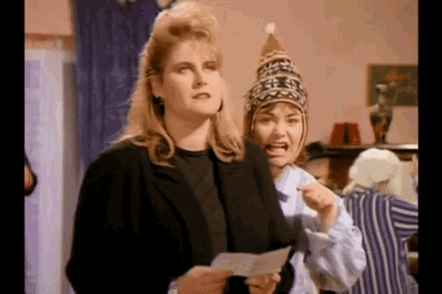 two women are standing next to each other and one of them is wearing a hat .