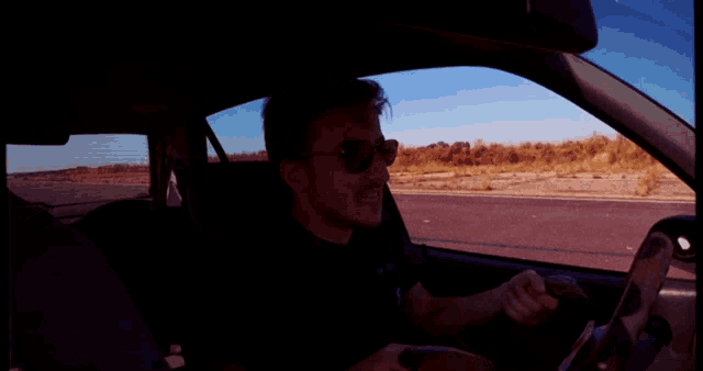 a man wearing sunglasses is driving a car and smiling