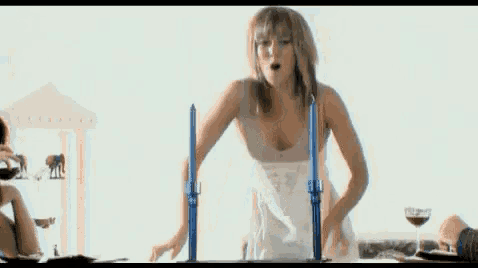 a woman in a white dress is standing in front of a table with candles on it .