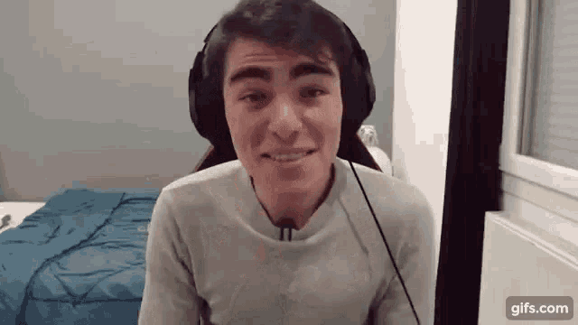 a young man wearing headphones is smiling in a bedroom .
