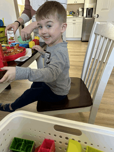 a little boy is sitting in a chair playing with blocks and a box of knorr