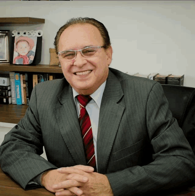 a man in a suit and tie is smiling in front of a bookshelf with a picture of a baby in a hat on it