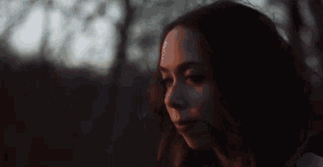a close up of a woman 's face in the woods at sunset .