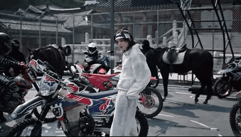 a woman standing in front of a row of dirt bikes and horses .