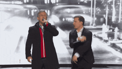 a man singing into a microphone while another man stands behind him