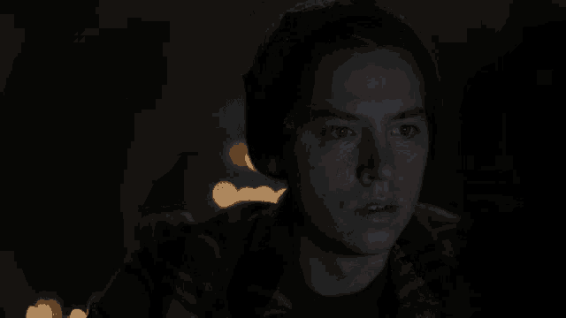 a man in a plaid shirt and a beanie looks at the camera in the dark