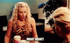 a woman sitting at a table with a cup of coffee says what what !