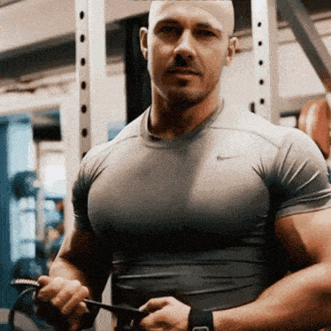 a bald man wearing a grey nike shirt is holding a rope