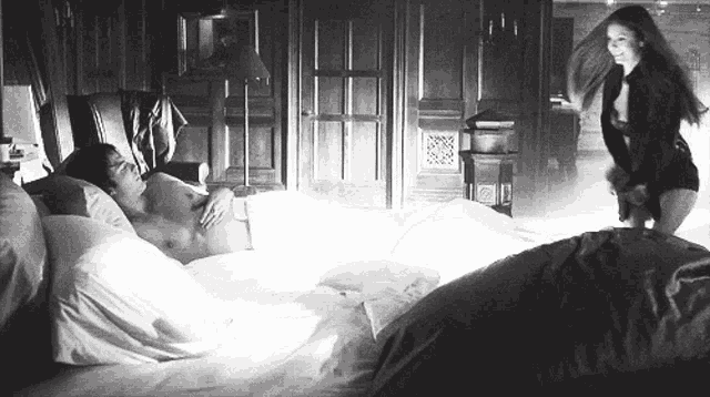 a woman is standing next to a man laying on a bed