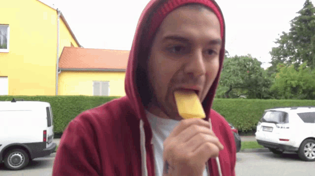a man in a red hoodie is eating a piece of fruit