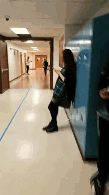 a woman in a plaid shirt is standing in a hallway next to blue lockers