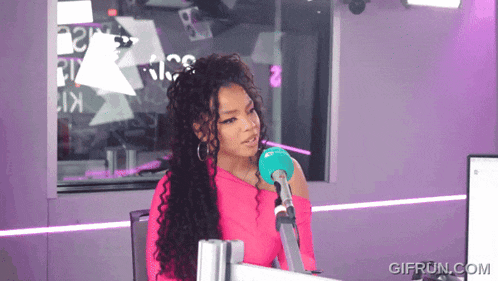a woman in a pink top is sitting in front of a microphone in a purple room .