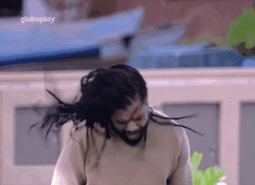 a man with dreadlocks and a beard is dancing in front of a sign that says globoplay
