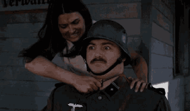 a woman is putting a helmet on a man with a mustache