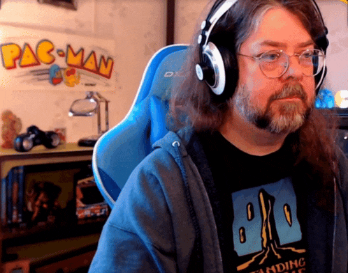 a man wearing headphones sits in front of a pac man poster