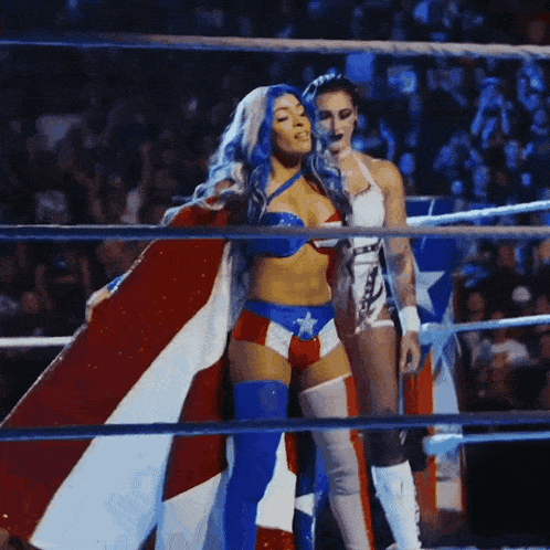 two women are standing in a wrestling ring one is wearing a cape