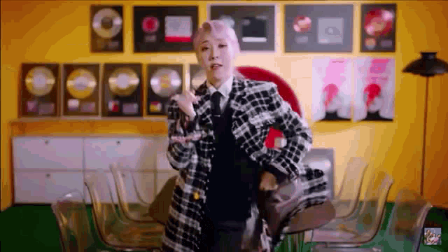 a woman in a plaid jacket and tie is dancing in a room with a lot of trophies on the wall .