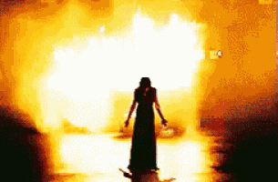 a woman in a long dress is standing in front of a fire