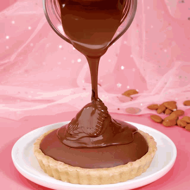 chocolate is being poured on a small pie on a white plate