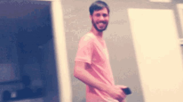 a man in a pink shirt is standing in a room holding a cell phone