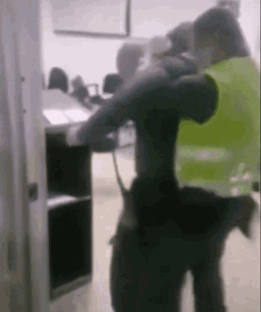 a man in a yellow vest is standing next to a man in a black shirt in a room .