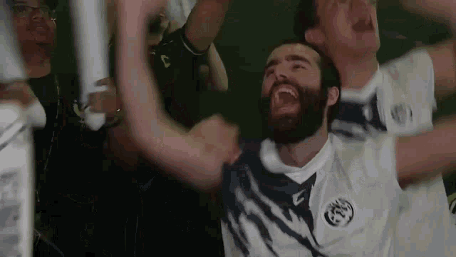 a man with a beard is laughing in front of a crowd while wearing a white shirt with the letter c on it .