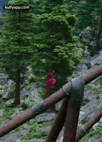 a woman in a red dress is hanging from a wooden bridge in the woods .