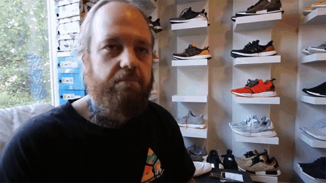 a man with a beard is sitting in front of a wall of sneakers
