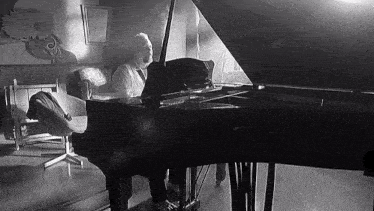 a black and white photo of a man playing a grand piano