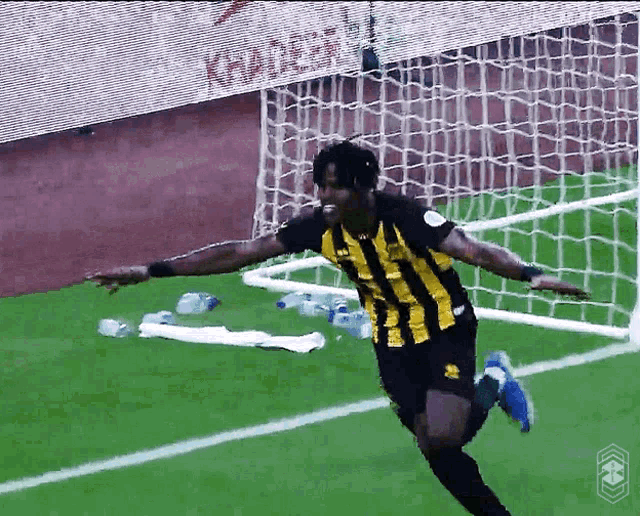 a soccer player in a black and yellow striped shirt is running towards the goal